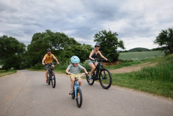 Young family with little child riding bicycles on road in village in summer.